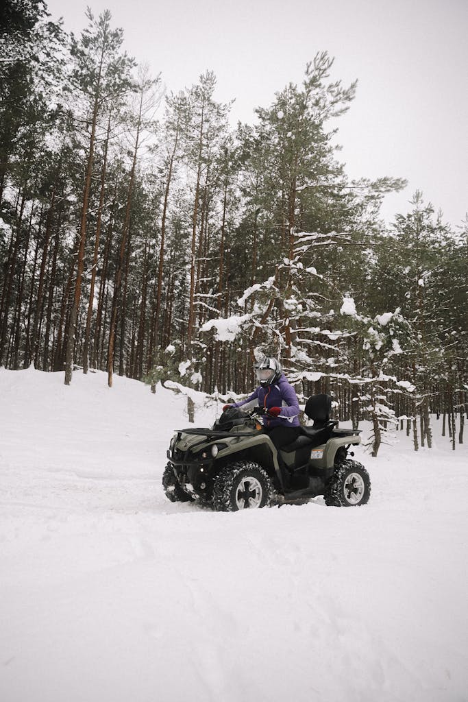 A person rides an ATV through a snow-covered forest in winter, showcasing off-road adventure.